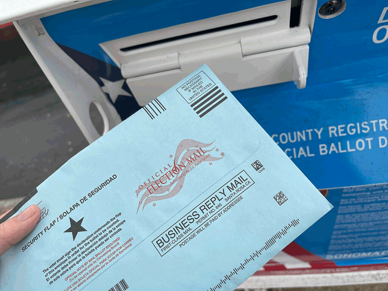 Image of a hand holding a ballot envelope in front of a ballot box